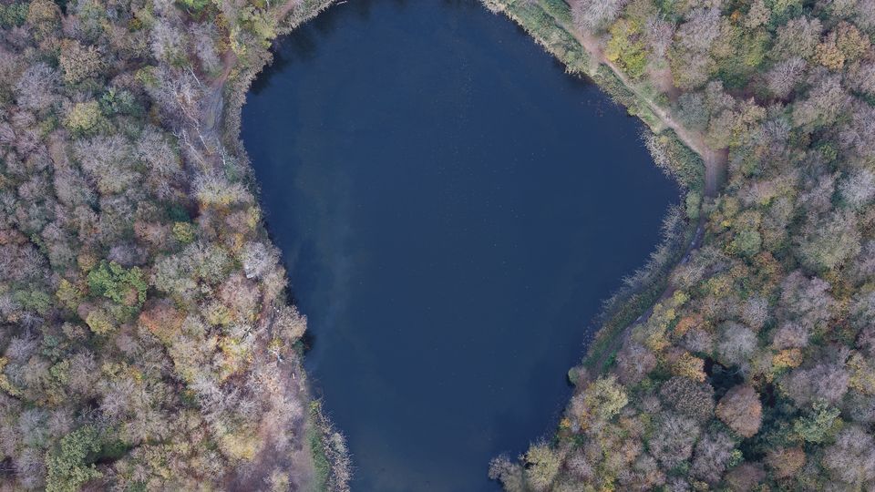Top-down drone view of a heart-shaped dark lake surrounded by autumn forest