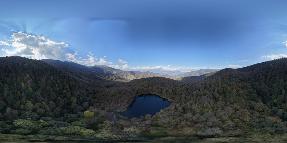 Aerial view of a small forest lake among autumn-coloured hills in Tavush, with mountains and cloud on the horizon